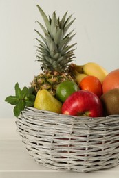 Photo of Fresh ripe fruits in wicker bowl on white wooden table, closeup