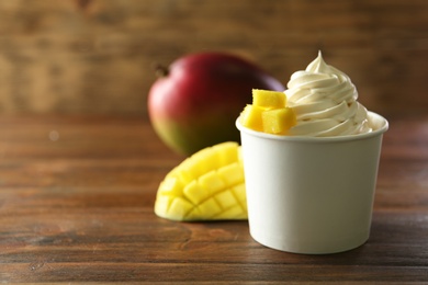 Cup of tasty frozen yogurt with mango on wooden table. Space for text