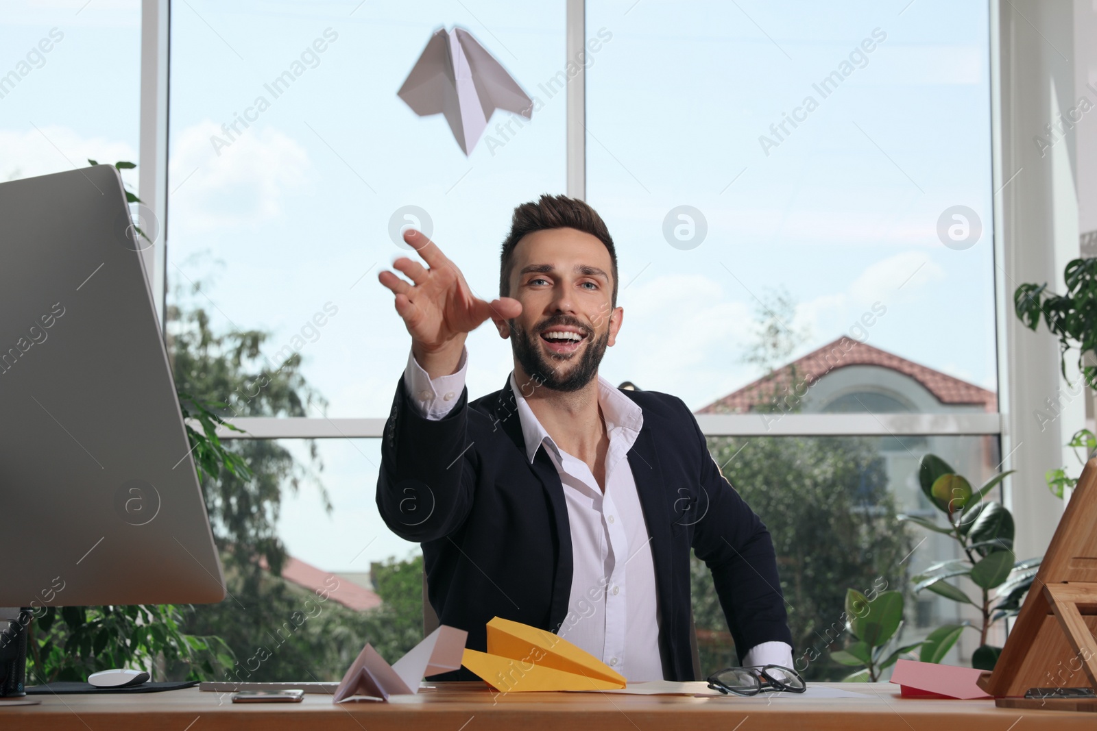 Photo of Handsome businessman playing with paper plane at desk in office