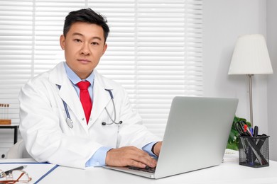 Photo of Doctor with laptop consulting patient at white desk in clinic. Online medicine