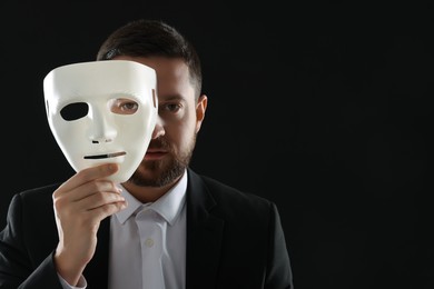 Photo of Multiple personality concept. Man covering face with mask on black background. Space for text