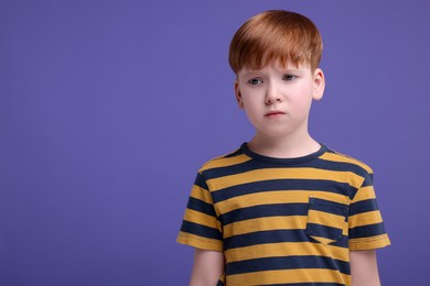 Portrait of sad little boy on purple background, space for text