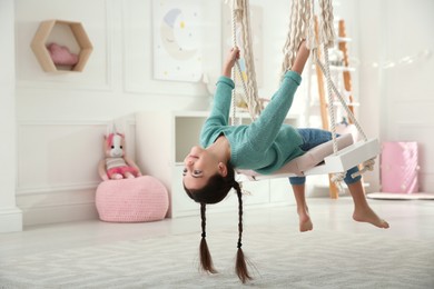 Cute little girl playing on swing at home