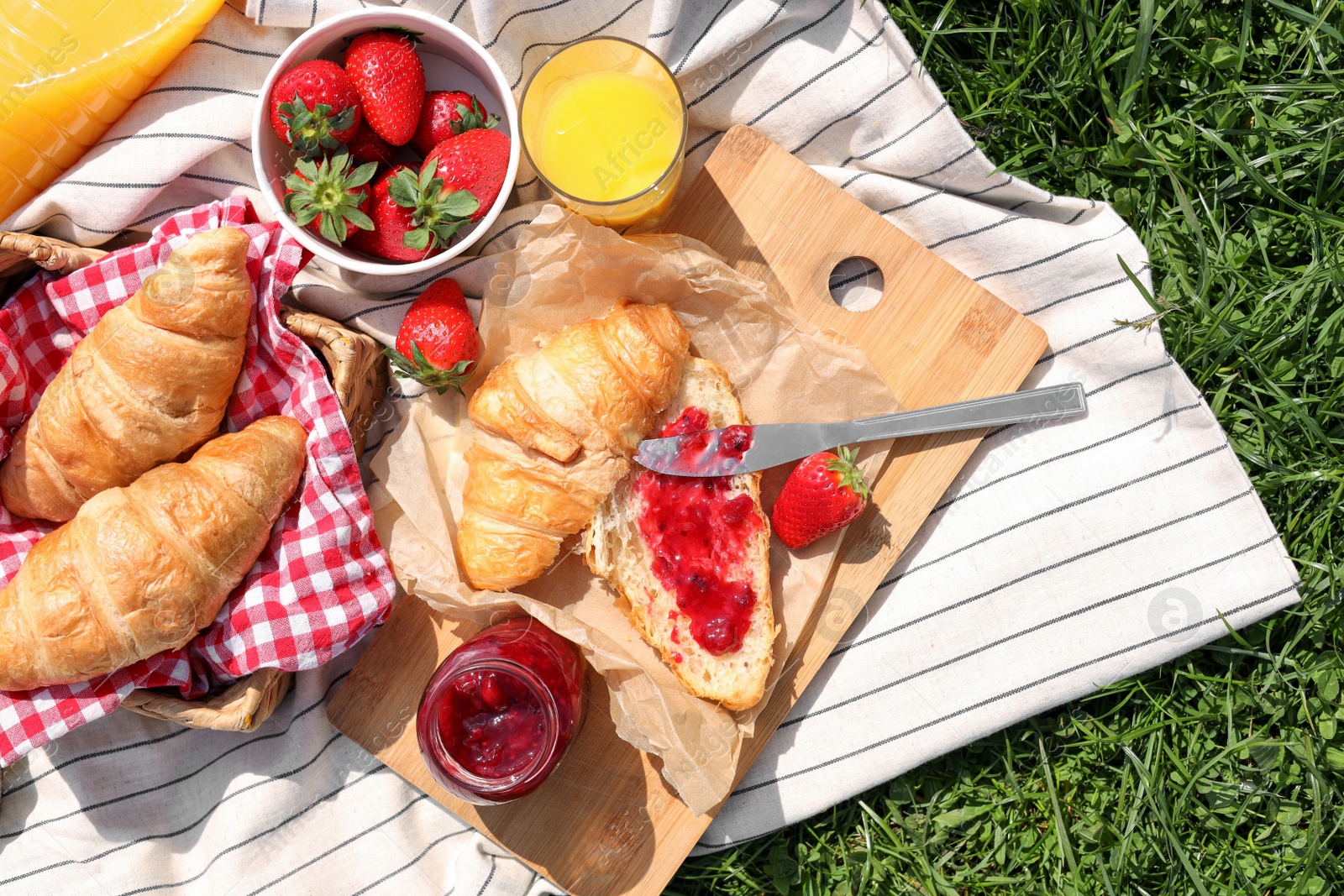 Photo of Blanket with different products on green grass, top view. Summer picnic