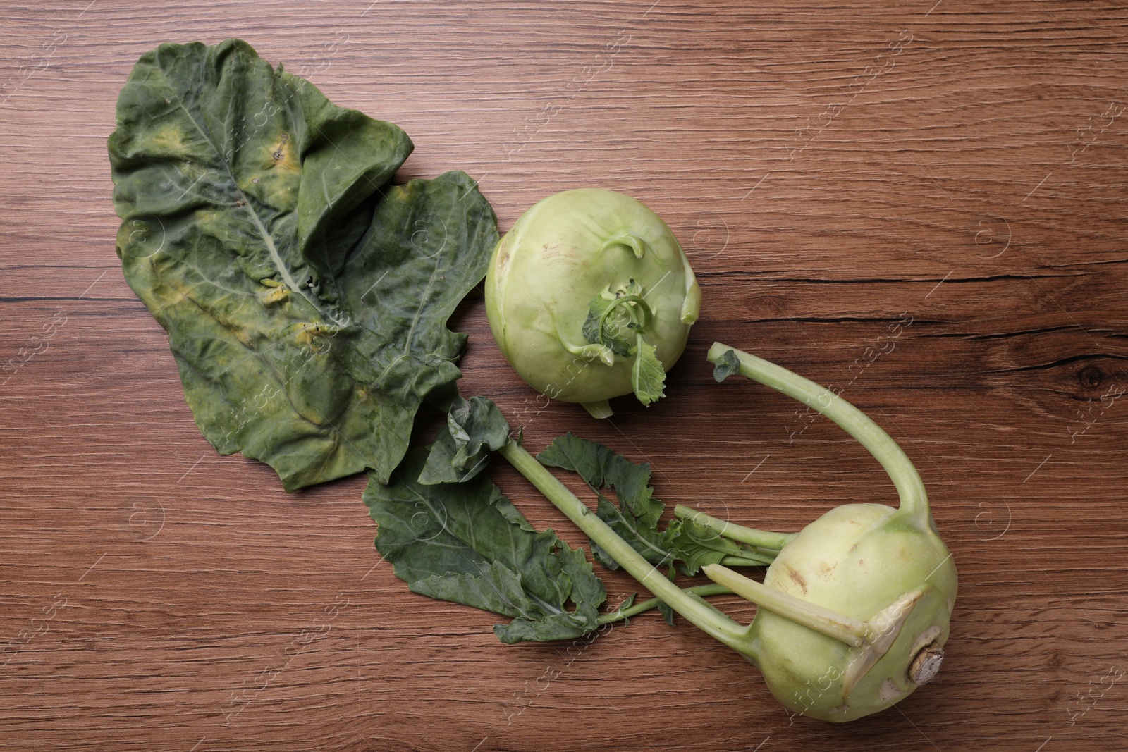 Photo of Whole ripe kohlrabies with leaves on wooden table, flat lay