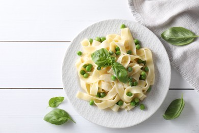 Delicious pasta with green peas and fresh basil on white wooden table, flat lay. Space for text