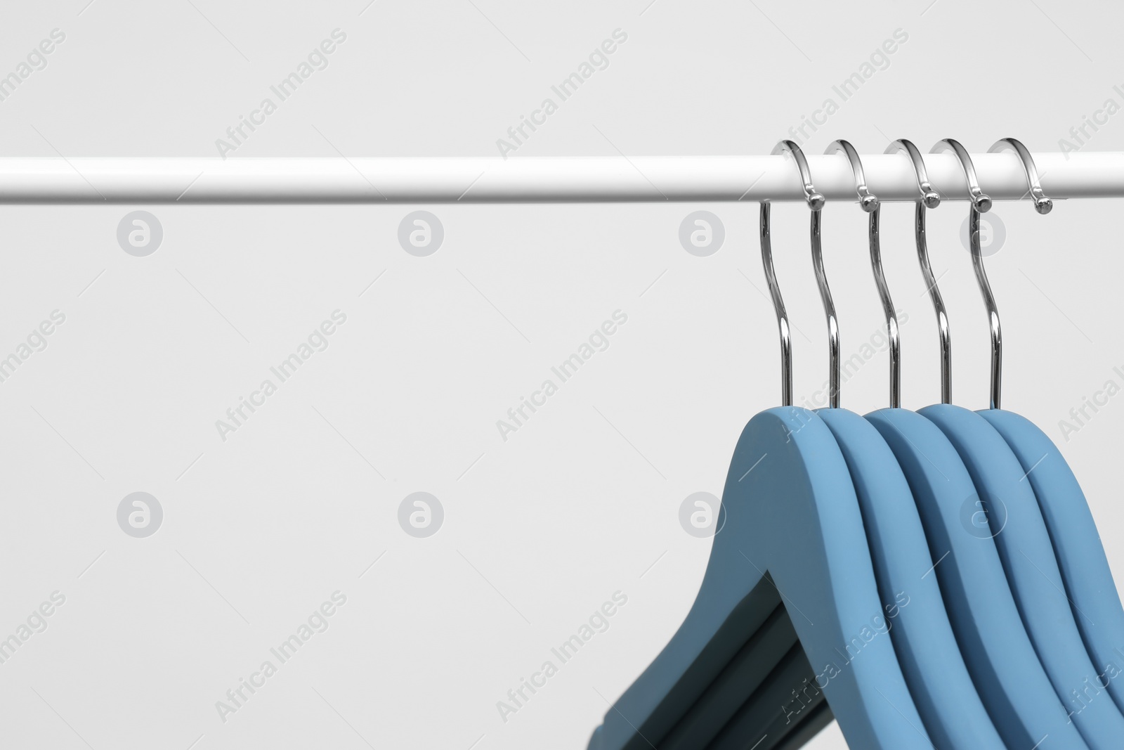 Photo of Empty clothes hangers on metal rail against light background, closeup. Space for text