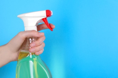 Photo of Woman holding plastic spray bottle on light blue background, closeup. Space for text