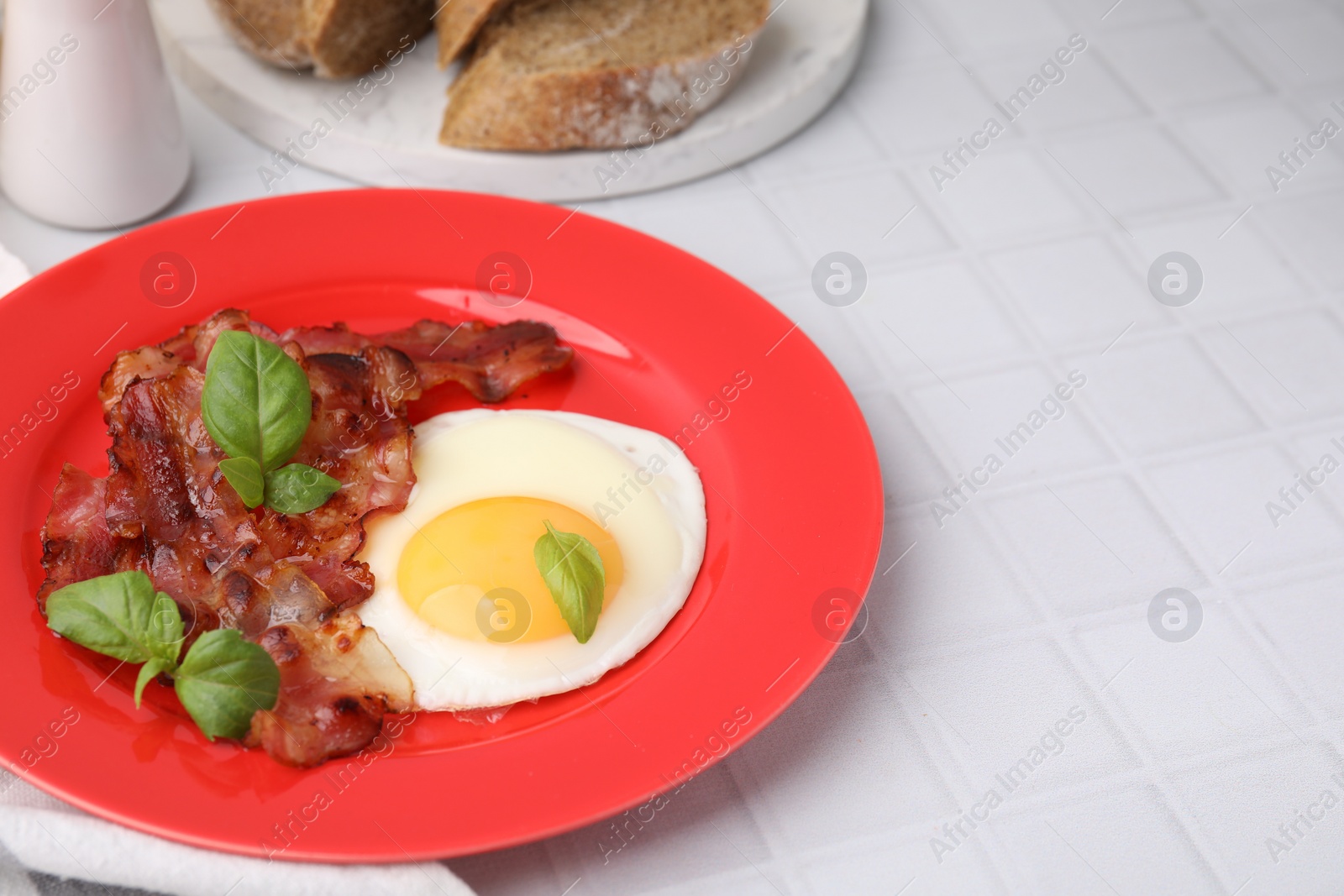 Photo of Fried egg, bacon and basil on white tiled table, space for text