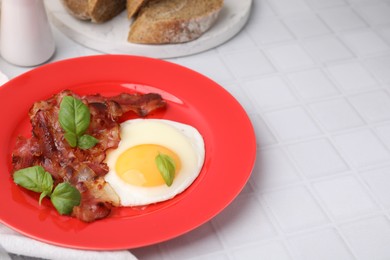 Photo of Fried egg, bacon and basil on white tiled table, space for text