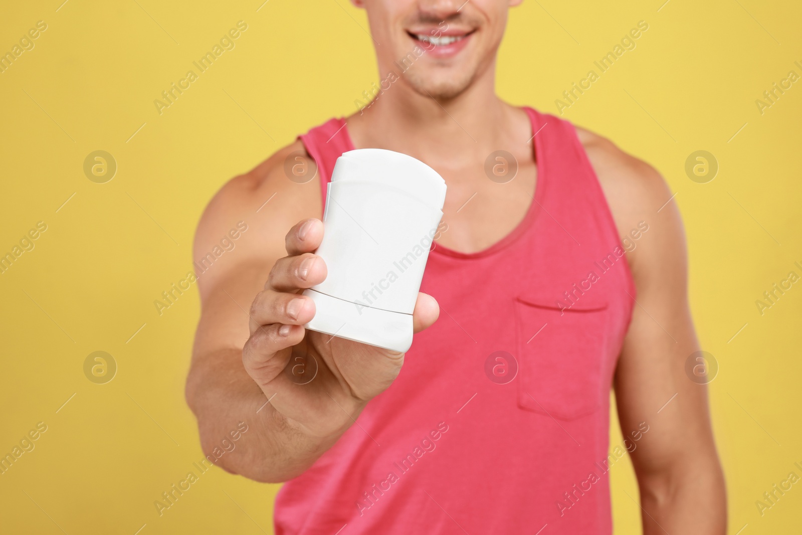 Photo of Young man with deodorant on yellow background, closeup