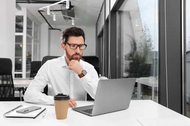 Photo of Man working on laptop at white desk in office. Space for text