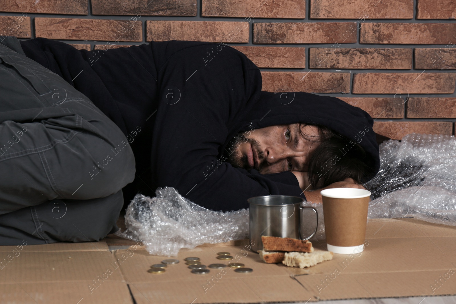 Photo of Poor homeless man lying on floor near brick wall