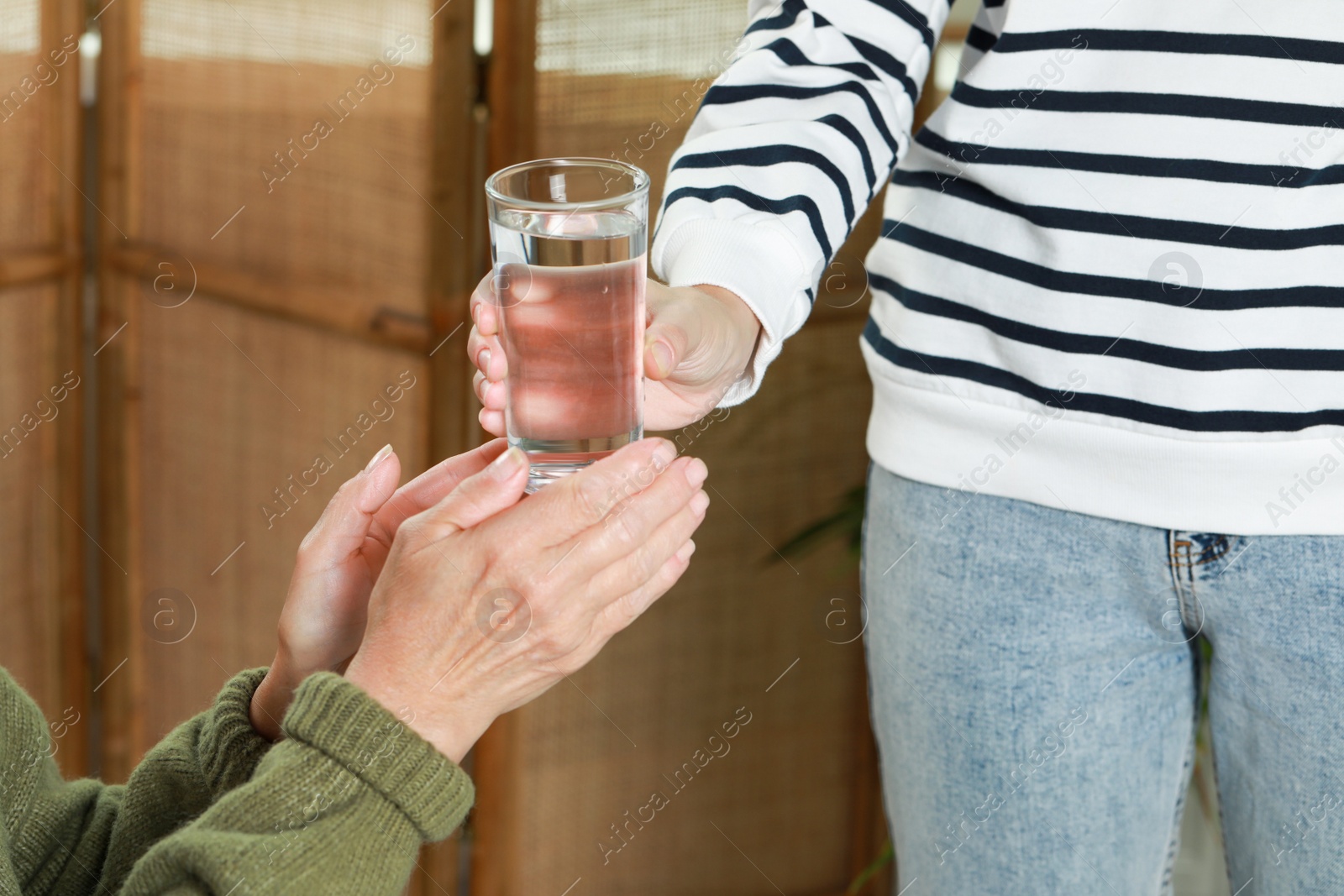 Photo of Caregiver giving water to elderly woman at home, closeup