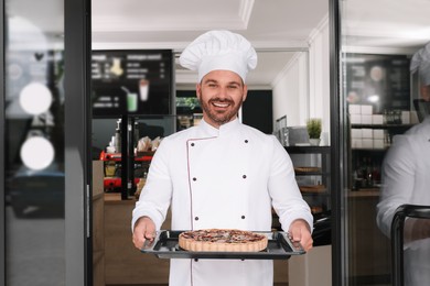 Happy baker presenting delicious quiche at door of his cafe