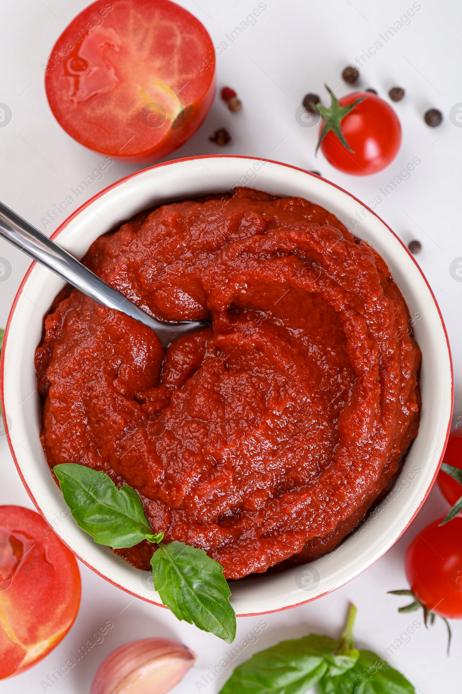 Photo of Tasty tomato paste in bowl and ingredients on white table, flat lay