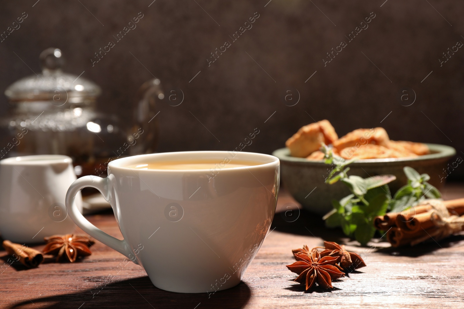 Photo of Cup of aromatic hot tea with milk and anise stars on wooden table