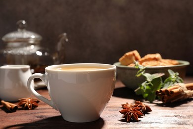 Cup of aromatic hot tea with milk and anise stars on wooden table