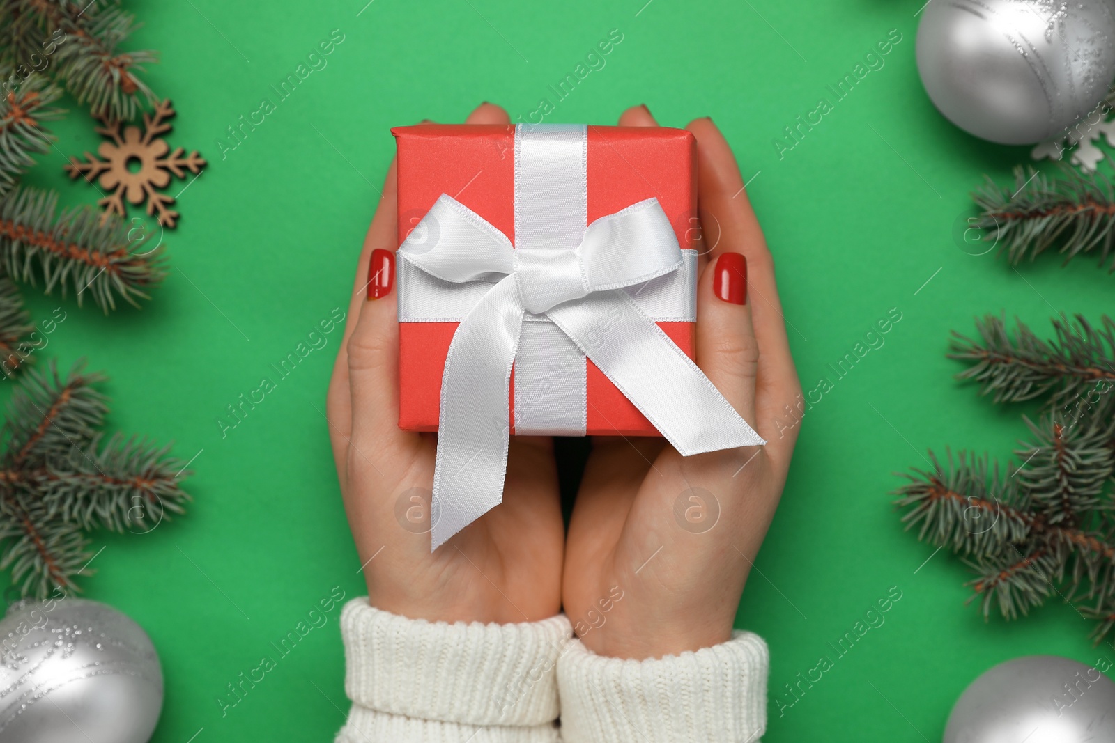 Photo of Woman holding gift box near fir tree branches with Christmas decor on green background, top view