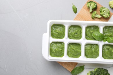 Photo of Broccoli puree in ice cube tray ready for freezing and ingredients on grey table, flat lay. Space for text