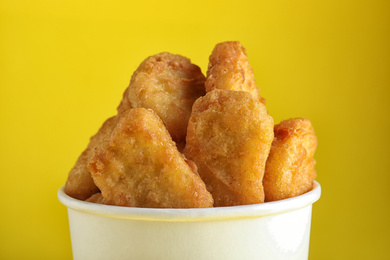 Bucket with tasty chicken nuggets on yellow background, closeup