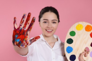 Photo of Woman with painted palm and palette on pink background, selective focus. Young artist