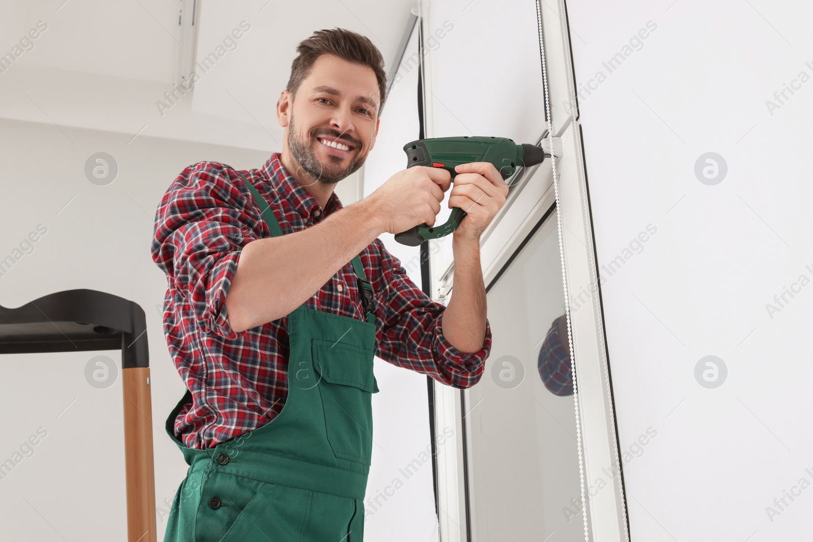 Photo of Worker in uniform installing roller window blind indoors