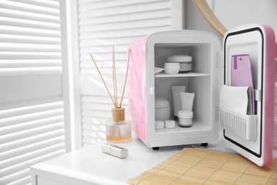 Photo of Cosmetics refrigerator and skin care products on white vanity table indoors