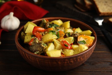Photo of Tasty cooked dish with potatoes in earthenware on wooden table