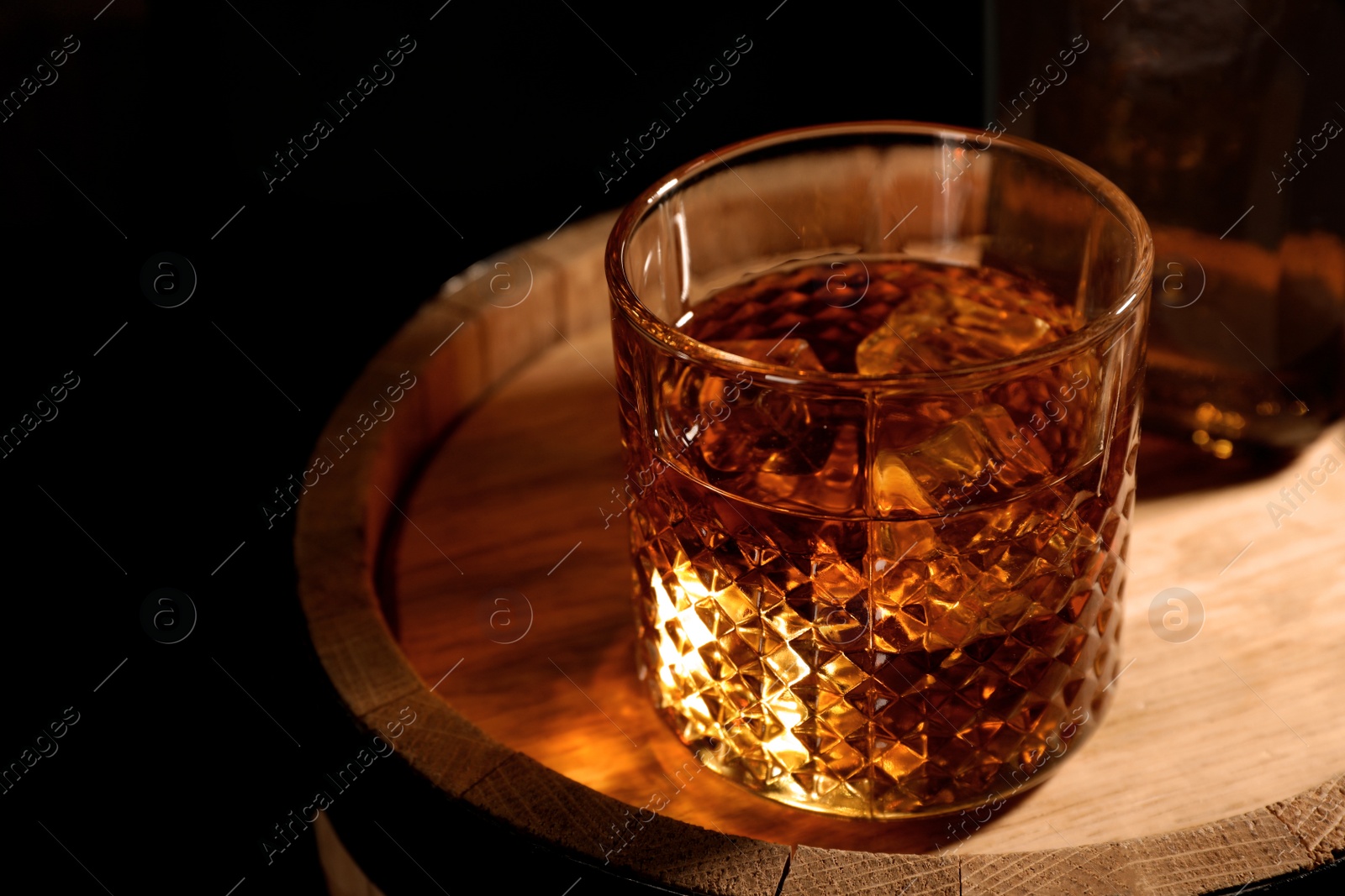 Photo of Golden whiskey in glass with ice cubes on wooden barrel. Space for text