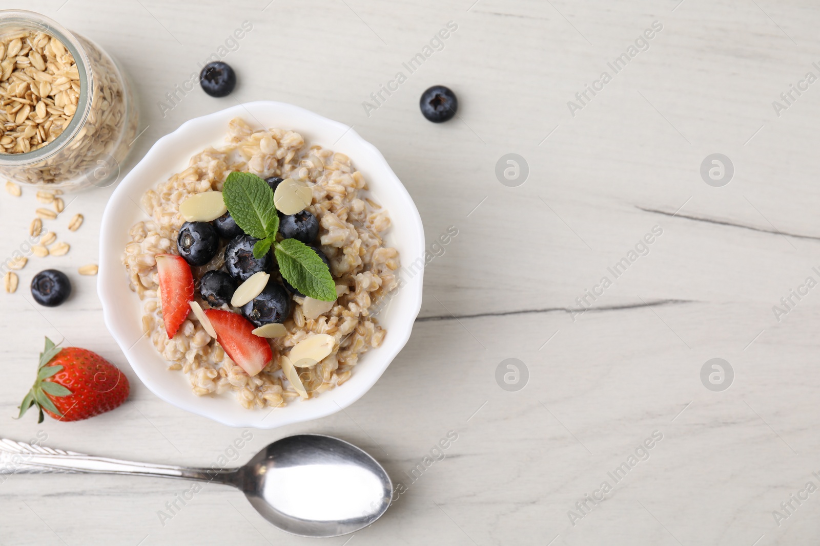 Photo of Tasty oatmeal with strawberries, blueberries and almond flakes in bowl served on white wooden table, flat lay. Space for text