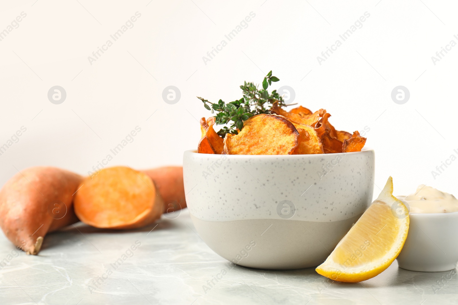 Photo of Bowl of sweet potato chips with sauce and lemon on table against white background. Space for text