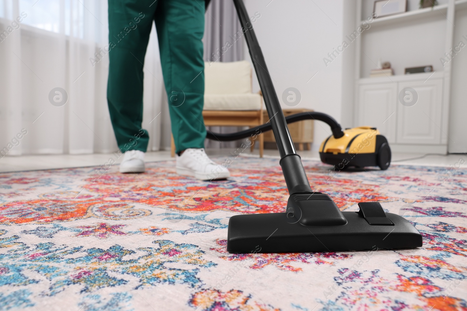 Photo of Dry cleaner's employee hoovering carpet with vacuum cleaner indoors, closeup