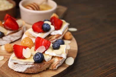 Tasty sandwiches with brie cheese, fresh berries and almond flakes on wooden table, closeup. Space for text