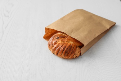 Paper bag with pastry on light wooden background. Space for text