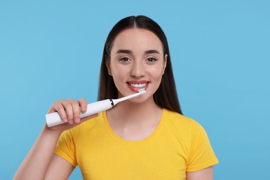 Photo of Happy young woman brushing her teeth with electric toothbrush on light blue background