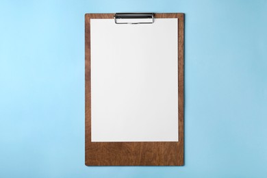 Photo of New wooden clipboard with sheet of blank paper on light blue background, top view