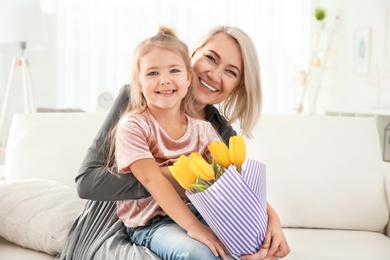 Photo of Cute little girl and her grandmother with tulip bouquet at home