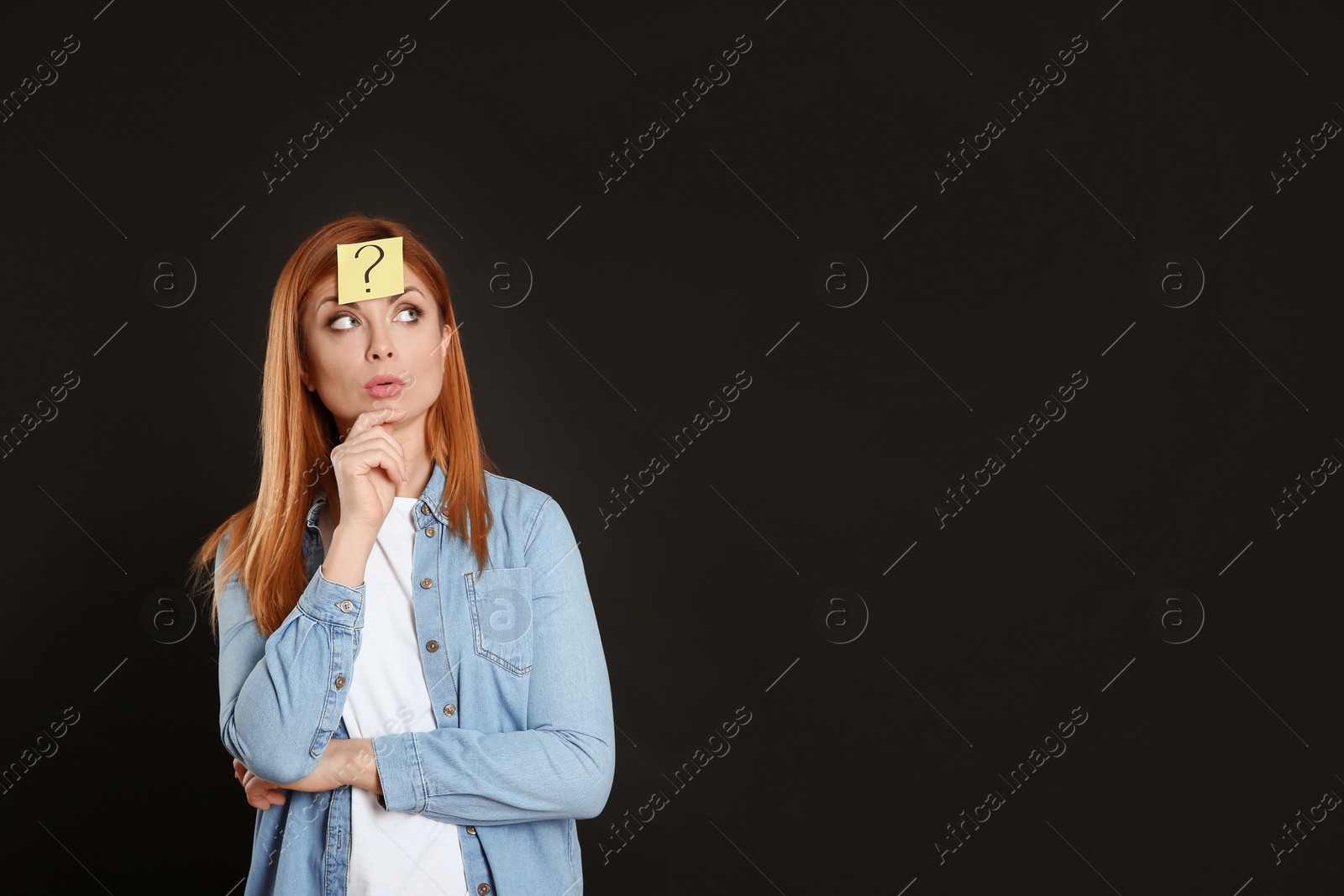 Photo of Pensive woman with question mark sticker on forehead against black background. Space for text