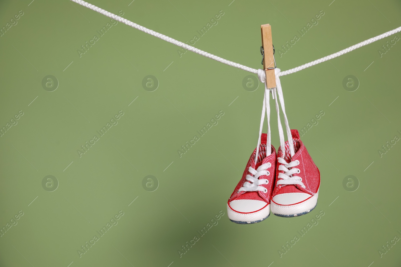 Photo of Cute small baby shoes hanging on washing line against green background, space for text