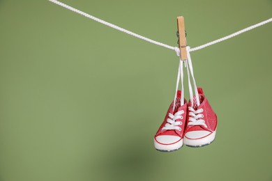 Cute small baby shoes hanging on washing line against green background, space for text