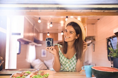 Photo of Young woman with vintage camera in trailer, view from outside. Camping vacation