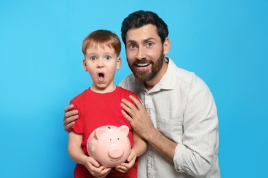 Photo of Father and his son with ceramic piggy bank on light blue background