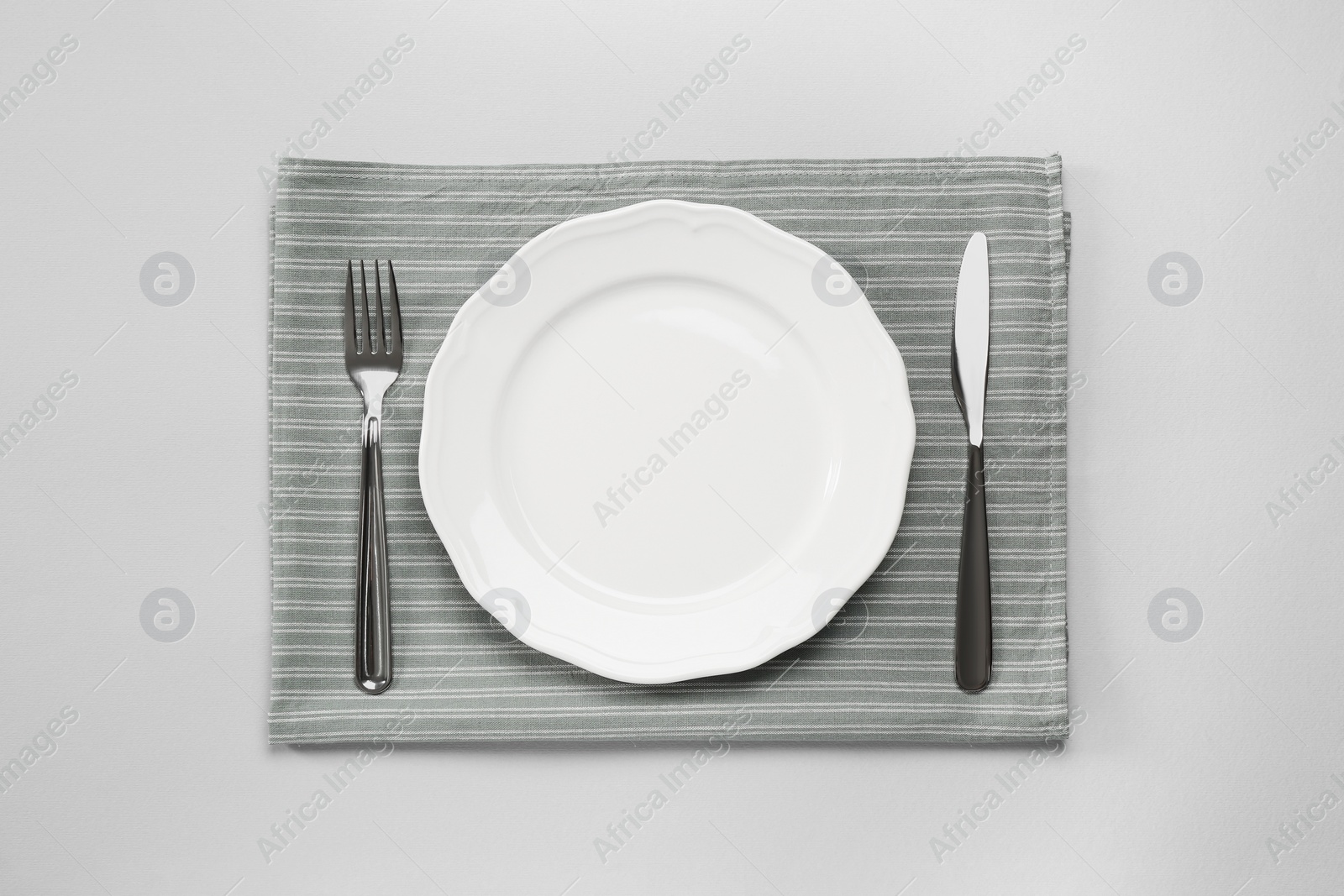 Photo of Clean plate and shiny silver cutlery on light grey background, flat lay