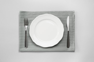 Photo of Clean plate and shiny silver cutlery on light grey background, flat lay
