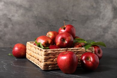 Photo of Fresh red apples and leaves in basket on dark grey table