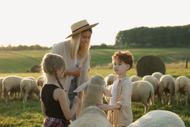 Photo of Mother and children stroking sheep on pasture. Farm animals
