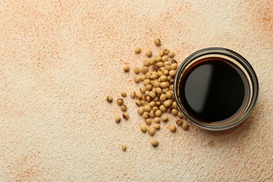 Photo of Soy sauce in bowl and beans on beige textured table, flat lay. Space for text
