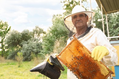 Beekeeper with smokepot and honey frame at apiary