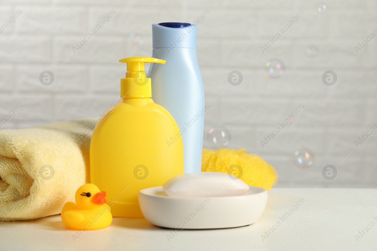 Photo of Baby cosmetic products, bath duck, sponge and towel on white table against soap bubbles. Space for text